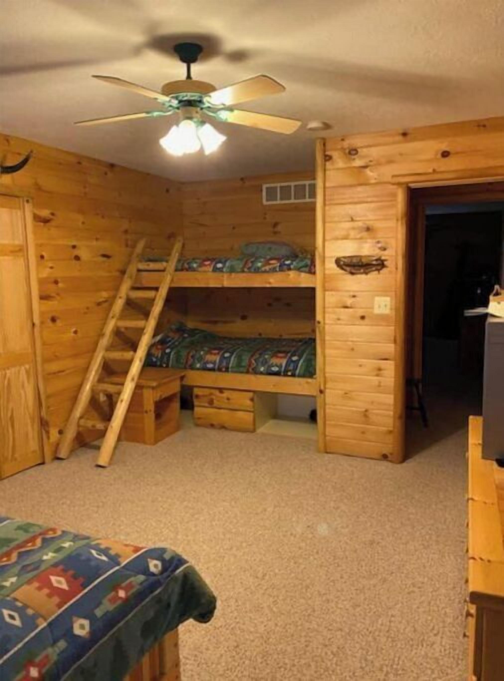 Een houten kamer met stapelbedden, een plafondventilator en een ladder.