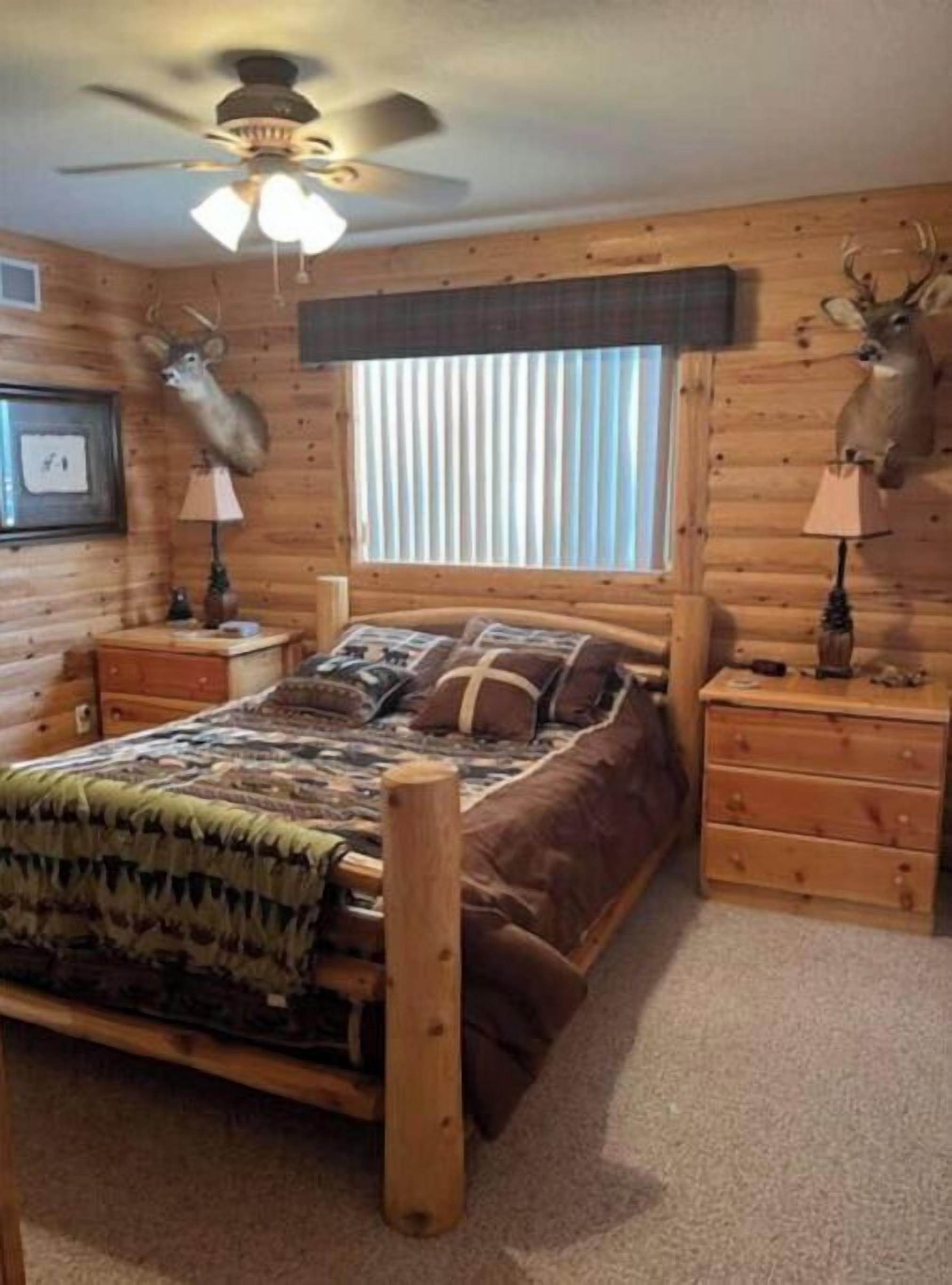 A log cabin bedroom with a bed, wooden nightstands, and deer antlers mounted on the walls.