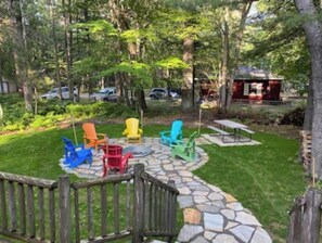 A stone patio with colorful Adirondack chairs, a wooden fence, and a stone pathway leading to a gazebo. - Cabin in Grayling, for all your activities near Lake Marguerite and more …… (Grayling)