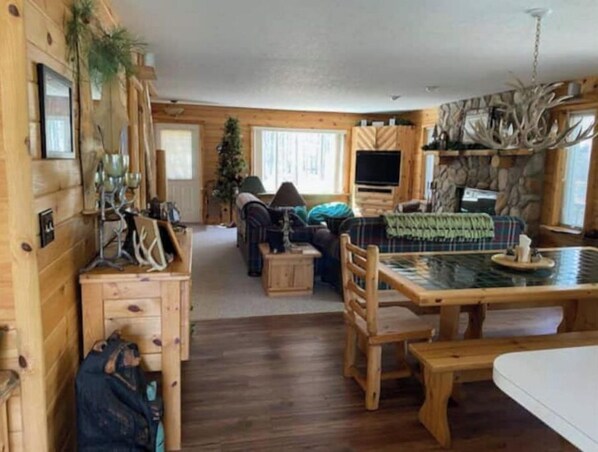 A cozy cabin interior with a wooden dining table, a sofa, and a fireplace. - Cabin in Grayling, for all your activities near Lake Marguerite and more …… (Grayling)