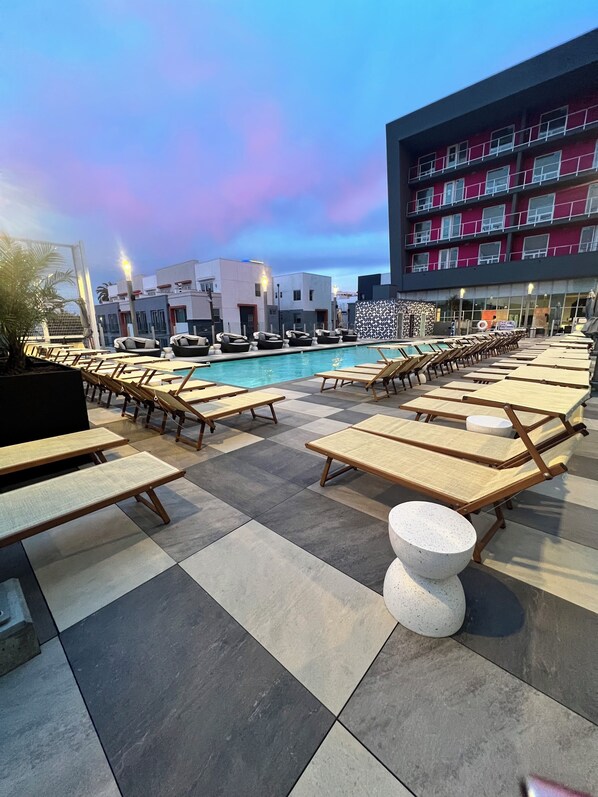 Relax by the pool surrounded by sun loungers and picnic tables on a spacious deck with a checkered pattern.