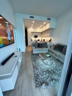 Cozy living space with a sofa, coffee table, and flat-screen TV, plus a compact kitchen area with modern appliances.
