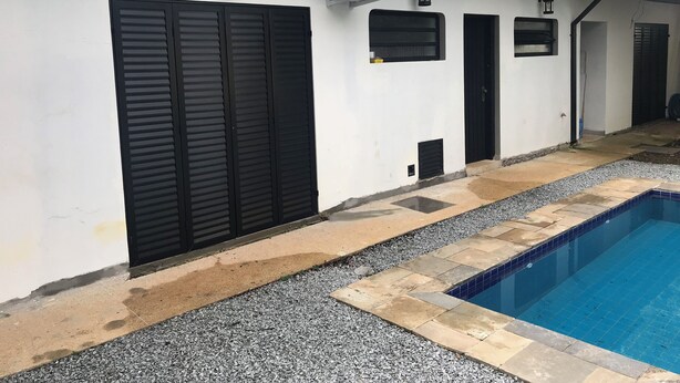 A poolside area with a swimming pool, a white wall with black shutters, and a tiled deck. - Colonial Hostel SP (São Paulo)