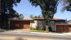 A street view with two garages, a fence, and a tree. - Colonial Hostel SP (São Paulo)