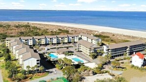 A beachfront hotel with multiple buildings, a swimming pool, and a beach in the background.