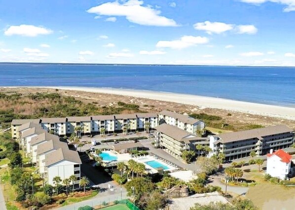 Un hotel frente a la playa con varias construcciones, una piscina y una playa al fondo.