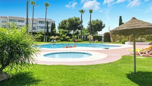 A swimming pool with two separate sections, surrounded by well-maintained grass and palm trees. - Garden Pool Apartment in Mijas by Costarentals - Ref 209 (Las Lagunas de Mijas)