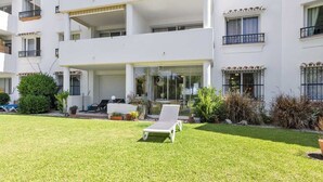 A multi-story residential building with a well-maintained lawn and a lounge chair. - Garden Pool Apartment in Mijas by Costarentals - Ref 209 (Las Lagunas de Mijas)
