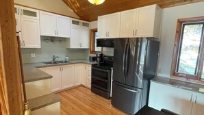 A modern kitchen with wooden flooring, white cabinets, a black refrigerator, and a built-in oven. - Beautiful Private Lakefront Home (Riondel)