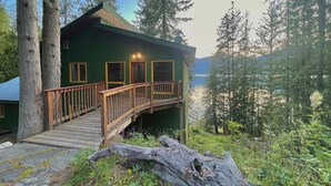A cabin with a wooden deck and a view of a lake surrounded by trees. - Beautiful Private Lakefront Home (Riondel)
