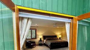A bedroom with a bed, bedside lamps, a chair, and a small table. - Beautiful Private Lakefront Home (Riondel)