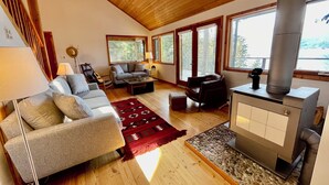 A cozy living room with a fireplace, wooden floors, and large windows. - Beautiful Private Lakefront Home (Riondel)