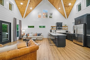 Una cocina moderna con una isla central, un área de comedor con sofá y un ventanal con vistas a zonas verdes.