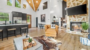 A spacious living area with a fireplace, a kitchen with a large island, and a dining area. - Romantic retreat, Hot tub, firepit and games! (Broken Bow)