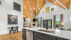 A modern kitchen with a large island, white cabinetry, and a stone accent wall. - Romantic retreat, Hot tub, firepit and games! (Broken Bow)