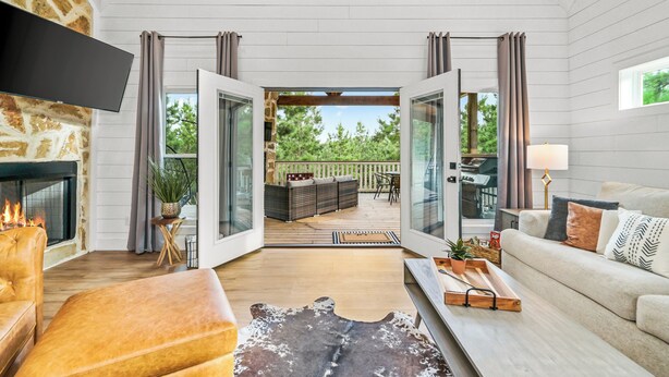 A spacious living area with a fireplace, a sofa, a coffee table, and a view of the outdoor patio. - Romantic retreat, Hot tub, firepit and games! (Broken Bow)