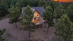A cabin with a stone foundation, wooden deck, and a staircase leading to the entrance. - Romantic retreat, Hot tub, firepit and games! (Broken Bow)