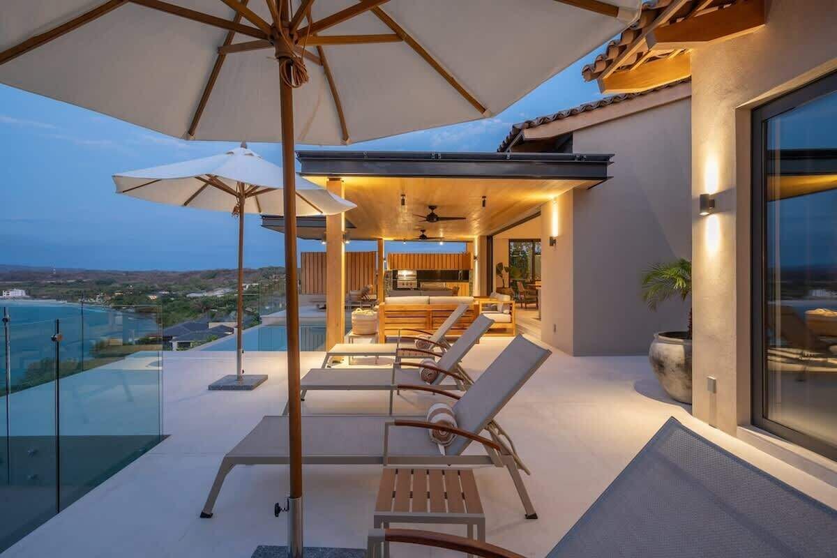 A modern outdoor patio with lounge chairs and umbrellas, overlooking a scenic view.