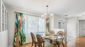 Un coin repas avec une table en verre, des chaises en osier et un rideau aux couleurs vives.