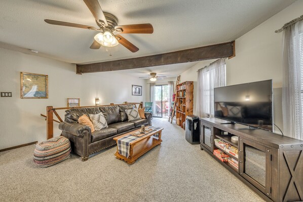 A living room with a leather sofa, a coffee table, a television on a cabinet, and a ceiling fan. - Ruidoso Home w/ Balcony ~ 16 Mi to Ski Apache! (Ruidoso)