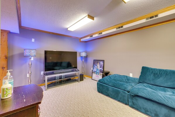 Una sala de estar con televisión de pantalla plana, dos lámparas, un sofá azul y un mueble de entretenimiento de madera.
