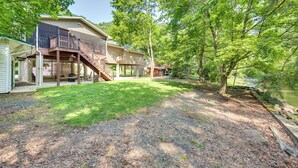 A two-story house with a covered porch and a deck, surrounded by trees and a gravel driveway. - Quaint Elysburg Cottage: Walk to Knoebels Resort! (Elysburg)