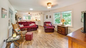 A spacious living room with a red sofa, a leather chair, and a wooden coffee table. - Quaint Elysburg Cottage: Walk to Knoebels Resort! (Elysburg)