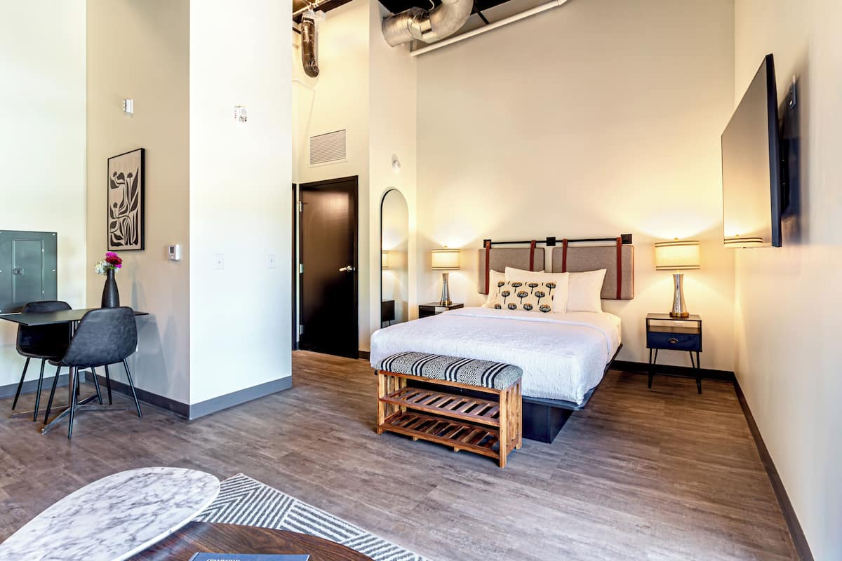 A modern hotel room with a bed, bedside tables, a desk, and a chair.