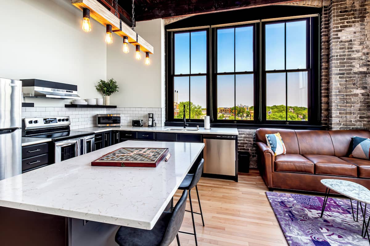 A modern kitchen with a large island, a dining area with a leather couch, and a large window with a city view.