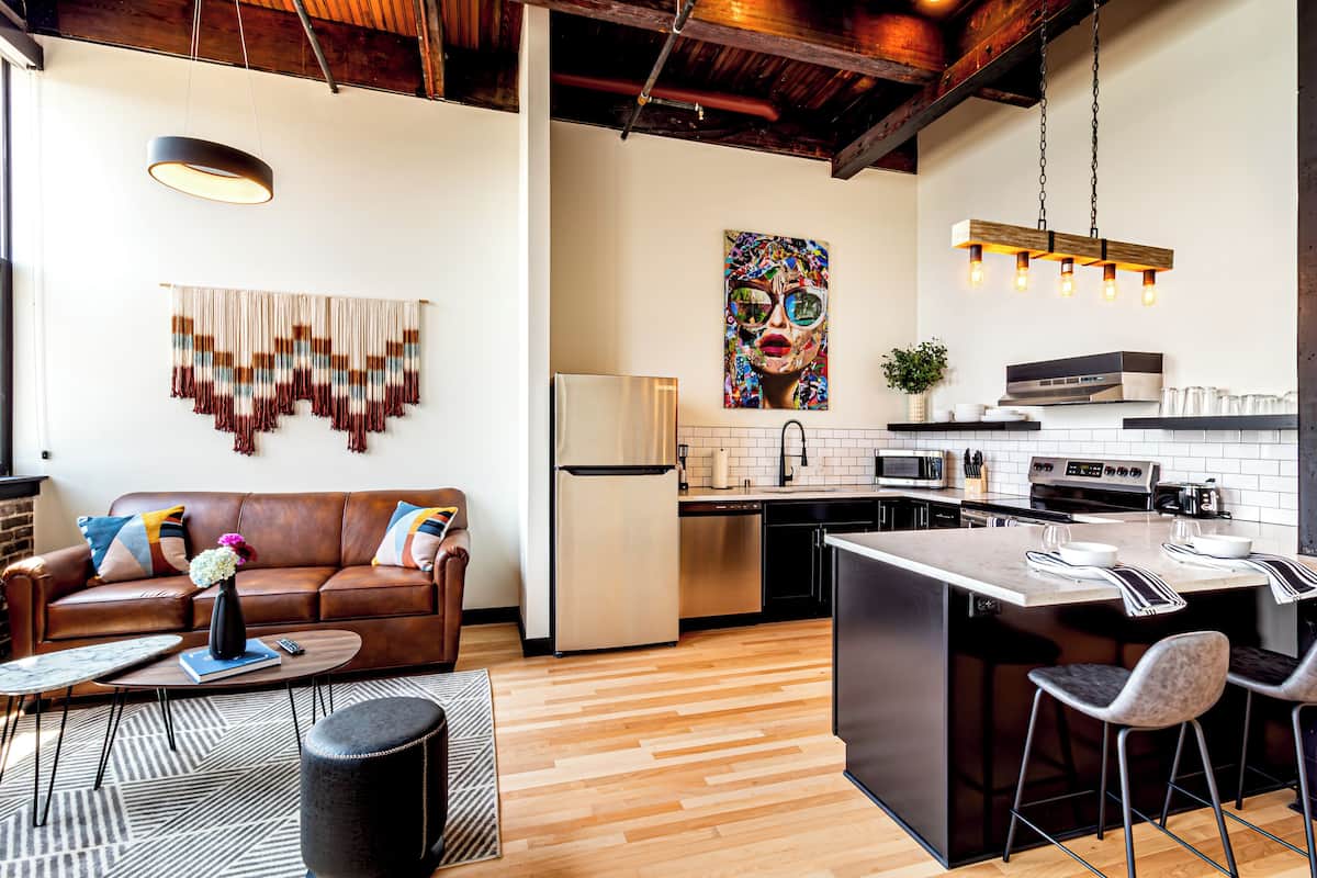 A modern kitchen with a central island, a dining area with a sofa and coffee table, and a living room with a fireplace.