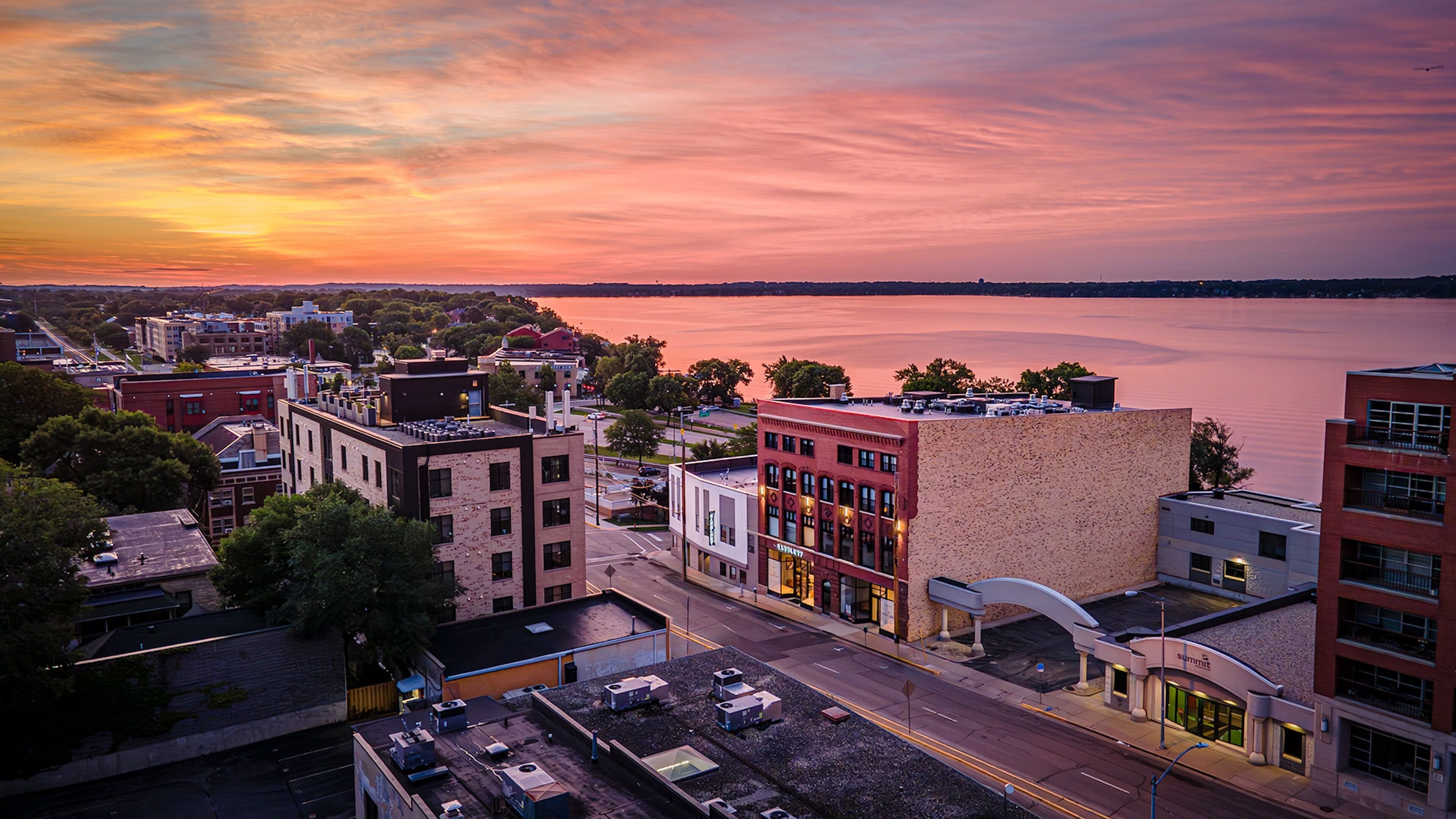 An urban landscape with buildings, a road, and a body of water during sunset.