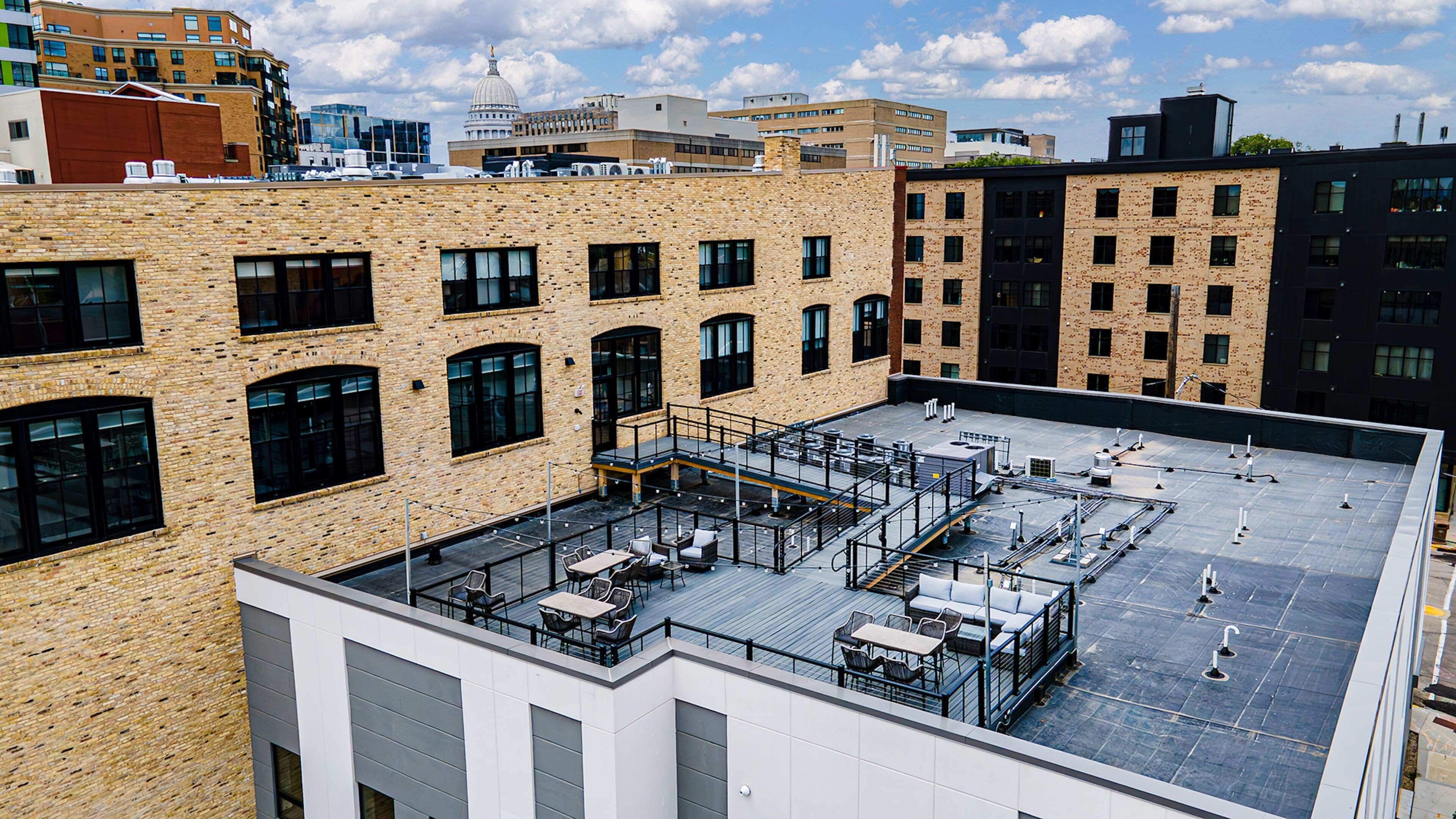 Una terraza en la azotea con mobiliario exterior, vistas al horizonte de la ciudad y fachada de un edificio de ladrillo.