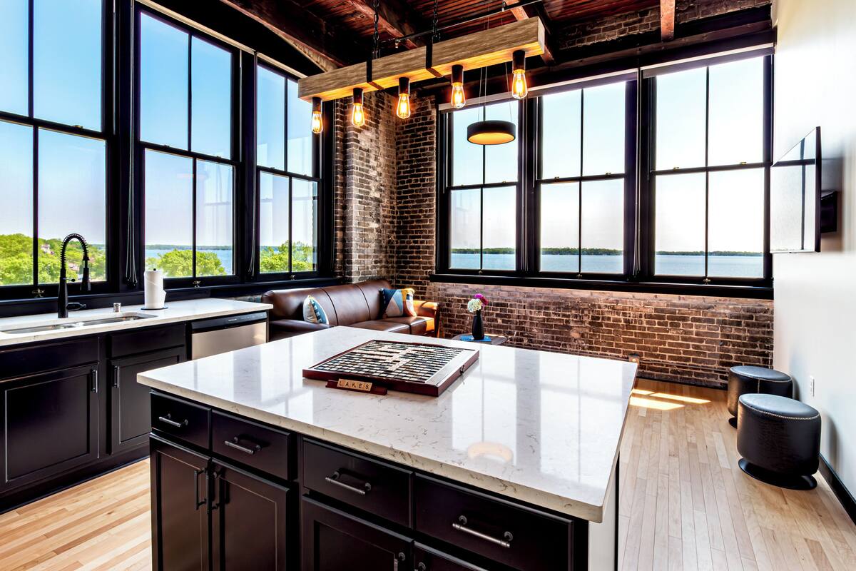 A modern kitchen with a large island, black cabinetry, and a view of a body of water through large windows.