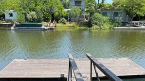 A wooden dock extending into a calm body of water with a small bridge connecting to a building in the background. - Dream Catcher Getaway (Clearlake Oaks)
