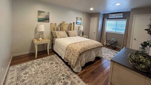 A bedroom with a bed, nightstands, a desk, a window with blinds, and a door. - Dream Catcher Getaway (Clearlake Oaks)