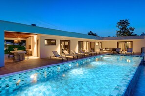 Un área de piscina moderna al aire libre con sillones de descanso y zona de comedor.