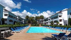A resort pool area with a clear blue pool, sun loungers, and white buildings with balconies. - Vacances EN Corse (San-Nicolao)