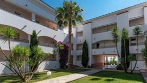 A multi-story building with balconies, surrounded by well-maintained grass and palm trees. - Vacances EN Corse (San-Nicolao)