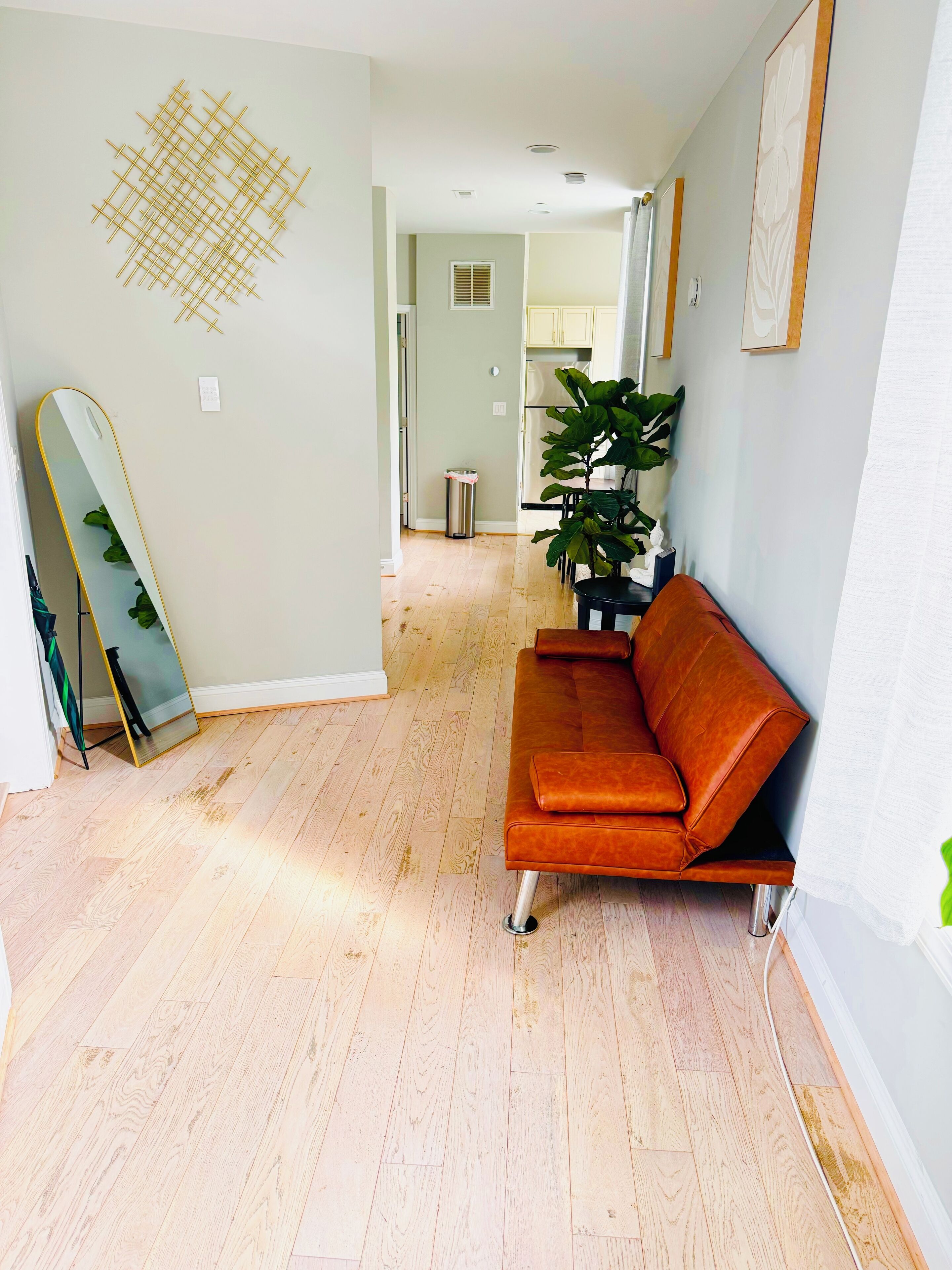 Ein modernes Wohnzimmer mit Holzboden, einem braunen Sofa, einem großen Spiegel und einem Blumentopf.