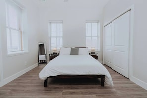 Un dormitorio con una cama, dos mesitas de noche con lámparas, un armario y un espejo.