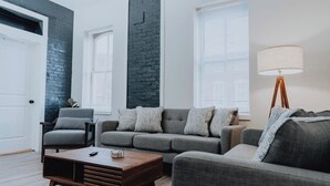 Een moderne woonkamer met een grijze bank, een houten salontafel en een vloerlamp.