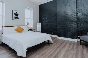 Une chambre à coucher avec un lit, une table de chevet, une lampe, une chaise, un mur en briques noires et une fenêtre.