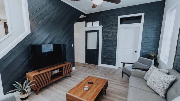 Een moderne woonkamer met een televisie, een houten salontafel en een grijze bank.