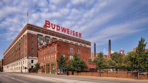 Een groot, bakstenen gebouw met het Budweiser logo, een opvallende schoorsteen en een heldere lucht.