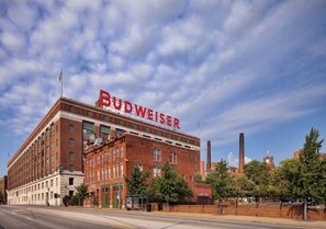 Een groot, bakstenen gebouw met het Budweiser logo, een opvallende schoorsteen en een heldere lucht.
