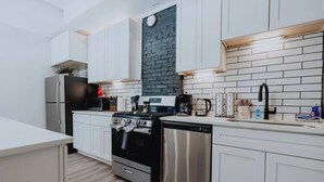 Een moderne keuken met witte kasten, een zwarte kookplaat, roestvrijstalen apparatuur en een accentmuur van baksteen.