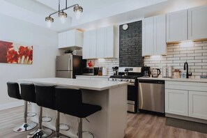 Une cuisine moderne avec des meubles blancs, un pare-feu noir, des appareils en acier inoxydable et un coin bar avec des tabourets.