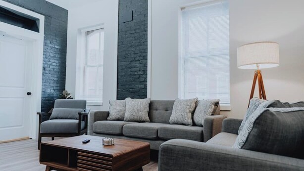 Een moderne woonkamer met een grijze bank, een houten salontafel en een vloerlamp.