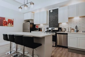 A modern kitchen with white cabinets, a black backsplash, stainless steel appliances, and a bar area with stools.