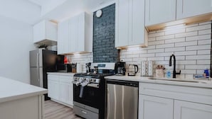 Een moderne keuken met witte kasten, een zwarte kookplaat, roestvrijstalen apparatuur en een accentmuur van baksteen.